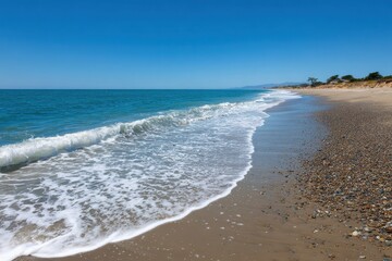 Gentle ocean waves kissing a pebble beach under a clear blue summer sky