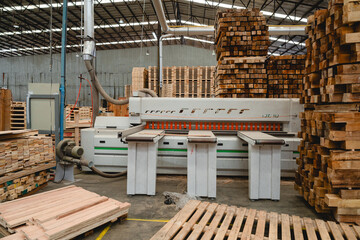 Automated wood cutting machine surrounded by stacks of lumber in a pallet warehouse, used for precision shaping in industrial production. Automated pallet manufacturing concept,