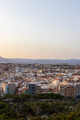 A scenic view of Alicante city showcasing a bustling urban landscape at dusk, featuring modern architecture and surrounding mountains, ideal for travel promotions.