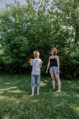 A mother and her son with hearing aids joyfully launch a paper airplane in a sunlit park, capturing a heartwarming moment of inclusive play and bonding in nature