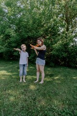 Obraz premium A mother and her son with hearing aids joyfully launch a paper airplane in a sunlit park, capturing a heartwarming moment of inclusive play and bonding in nature