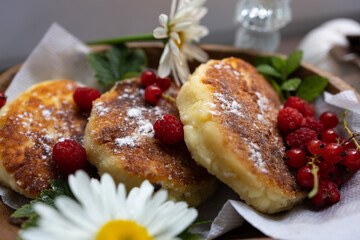 golden cheesecakes on a wooden plate with fresh raspberries and mint leaves. Decorated with white daisies, the atmosphere of a rustic breakfast.