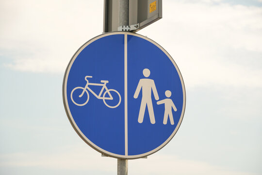 A circular road sign features symbols of a bicycle and a walking adult with a child, indicating a shared pathway for cyclists and pedestrians in a serene outdoor environment