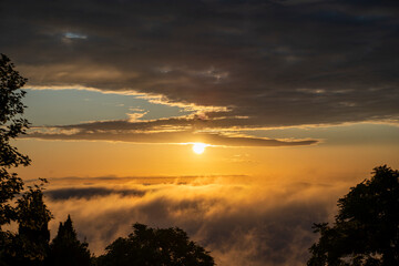 golden sunset over the clouds or fog of tuscany in a view from Montepulciano into the backlight of the going sun with silhouettes of trees