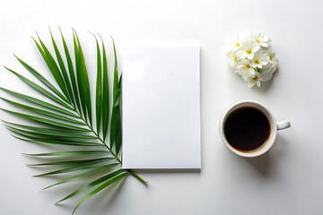 A blank notebook is displayed with a cup of coffee, white flowers, and a palm leaf on a white surface