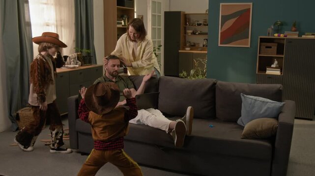 Woman playing with two sons wearing costumes when her husband working on laptop sitting on couch, he complaining about noise, she asking sons to be quiet and leaving with them