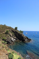 Fototapeta premium Coastal landscape near Plage des Oursins, Pyrénées-Orientales, France featuring winding coastal path, clear tranquil mediterranean sea waters with boats visible nearby