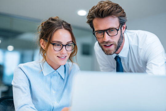Two colleagues collaborating and smiling while looking at a laptop screen in an office