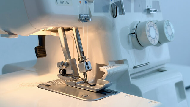 Overlock, sewing machine, with needle and white threads, on a white background, close-up. A white sewing machine with a silver needle.