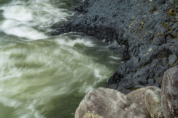 textures of the power of water between black volcanic rocks in a river that is turquoise and green in color