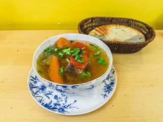 Uzbek shurpa soup with lamb carrots cilantro and flatbread on wood table before yellow wall