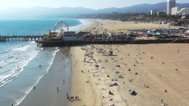 Aerial View of Santa Monica Pier in Santa Monica, CA in the Summer. The Drone POV Shows the Ferris Wheel and Roller Coaster. Malibu California and the Pacific Ocean Brings Tourists to the Beach