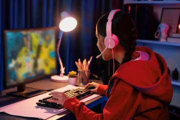 Obraz premium Host channel of young beautiful Asian gaming streamer playing fighting Moba at battle arena game on pc screen with multiplays, wearing pastel headphone at neon digital light modern room. Stratagem.