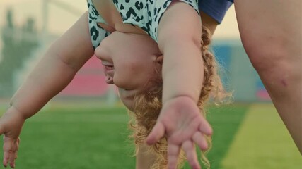 A child is playfully hanging upside down supported by an adult The cheerful atmosphere captures laughter and fun set on a vibrant green sports field under the sun