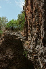 Upward view of weathered limestone cliff face with reddish rock coloring and sparse vegetation growing in cracks