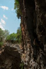 View from inside limestone cave looking up at blue sky through natural opening with surrounding vegetation