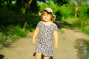 A small child strolls down a countryside path wearing a comfortable dress and a cute hat The...