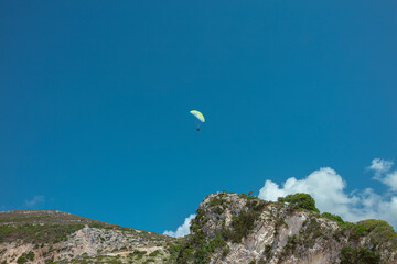 Single paraglider with green wing soaring above limestone mountains in clear blue sky