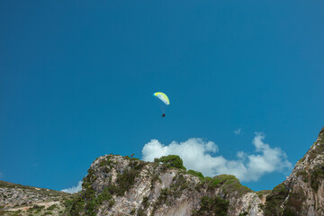 Single paraglider with yellow-green wing against clear blue Mediterranean sky