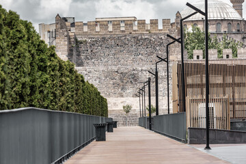 Modern wooden walkway and trimmed hedges in the inner yard of Kayseri citadel with historic stone walls and mosque dome, Turkey
