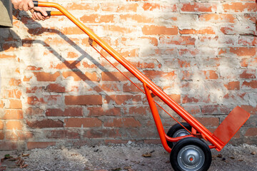 Man with hand truck near brick wall. Device with platform for transporting cargo