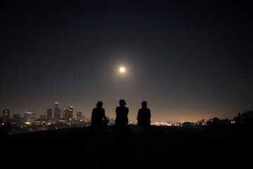 Three friends silhouetted against moonlit city skyline, sharing a moment