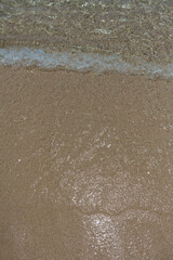 Gentle waves meeting sandy shoreline with foam and bubbles creating natural beach texture patterns