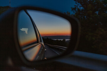 Car side mirror reflecting beautiful sunset landscape and coastal scenery during evening travel