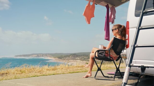 Enjoying a peaceful moment by the coastline while sipping a beverage, with clothes hanging to dry on a camper van.