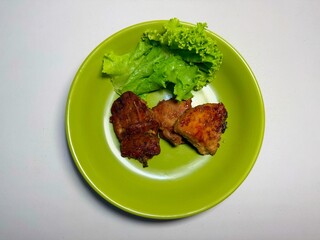 Three pieces of grilled or roasted meat are served on a vibrant green plate with fresh lettuce. This overhead shot is ideal for food bloggers, recipe websites, or restaurant menus