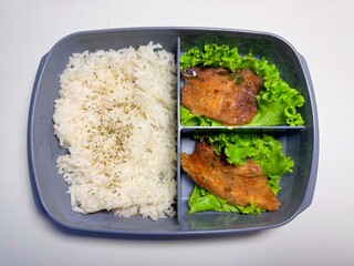Asian lunch box with steamed rice and grilled meat on fresh lettuce. Healthy homemade meal in plastic container, ideal for food delivery, diet plan, or bento concept
