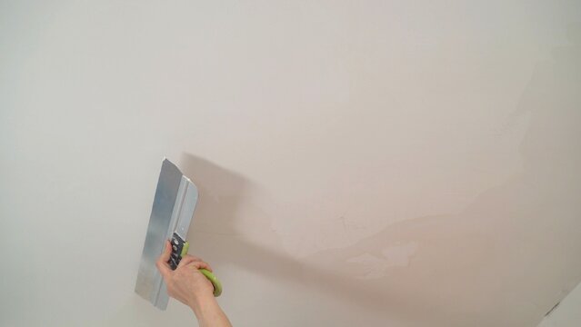 Construction worker is using spatula to apply plaster on white ceiling, performing home renovation work - Powered by Adobe