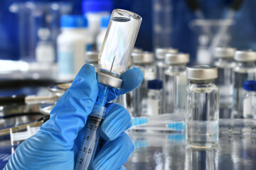 Medical personnel filling a syringe needle with generic vaccine booster from vial