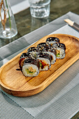 An exquisite presentation of sushi rolls featuring vibrant ingredients, garnished with sesame seeds and a glossy sauce on a wooden platter.