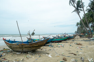 Fototapeta premium Trash-Littered Beach with Fishing Boats in Vietnam
