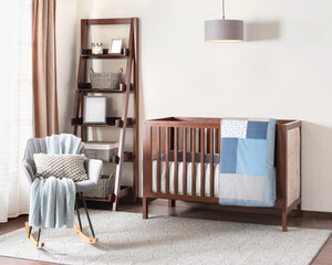 Cozy baby nursery featuring a wooden crib with blue patchwork quilt, a modern gray rocking chair...