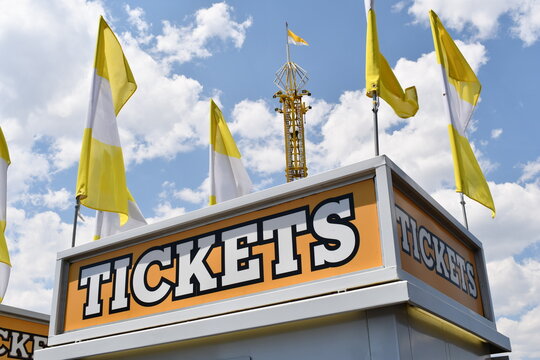 Ticket booth at carnival. Bright white letters against orange background. Tower in background.