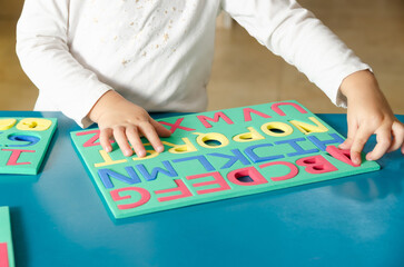 A little girl playing with colorful foam letters, numbers and geometric shapes on a blue table. 