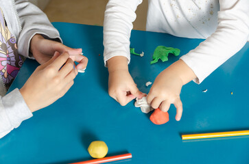 Two little sisters playing with colorful modeling dough on a blue table. 