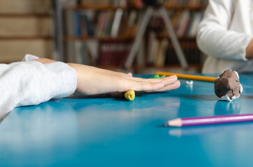 Two little sisters playing with colorful modeling dough on a blue table. 