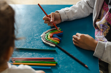Two little sisters making a rainbow with colorful modeling dough and playing with some pencils.