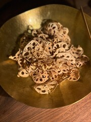 Close-up of crispy lotus root chips served in a golden bowl on a wooden table. Aesthetic food photography ideal for healthy snack, plant-based diet, or gourmet content themes.