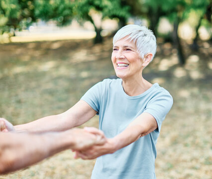 Happy active senior couple, portrait of an elderly woman with her husband dancing or swinging and holding hands and exercising in park outdoors