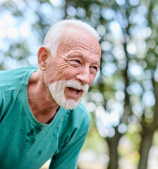 Portrait of a mature senior man exercising in a park, tired mature male running and taking a break...