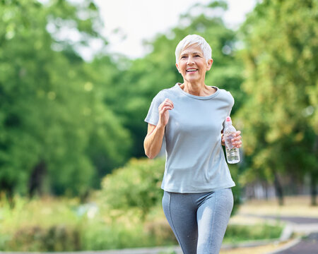 Smiling active mature elderly woman jogging running and holding a water bottle  in the park