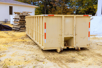 Large waste container sits on construction site surrounded by wooden pallets debris during works day hours.