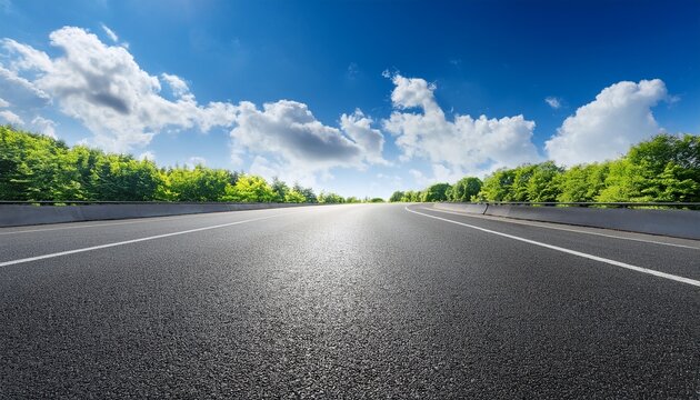 empty asphalt road under a bright blue sky with fluffy white clouds and green trees in the background