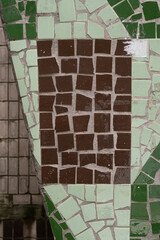 Brown square tile mosaic bordered with irregular green ceramic fragments on a wall.