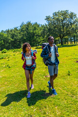 Hikers walking in green meadow by forest on sunny day