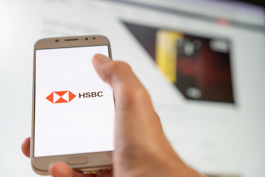 Person holding smartphone displaying HSBC logo with blurred background of computer screen for digital banking